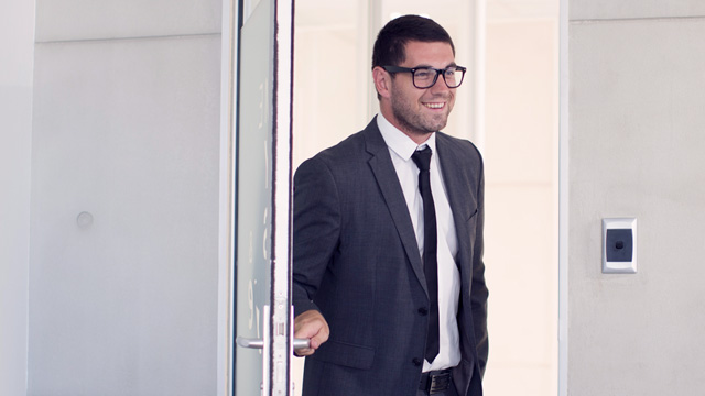 Man in suit entering an office while smiling